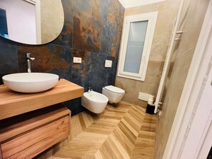 A modern bathroom with a round mirror, a wooden vanity, a white sink, a bidet, and a toilet. - New Listing (Sanremo)