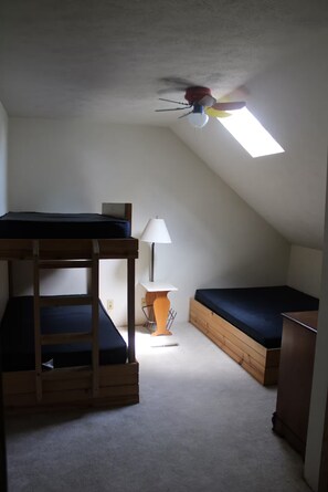Une chambre de dortoir avec des lits superposés, un bureau, une lampe et un ventilateur de plafond.