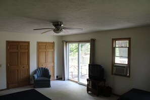 Une pièce dotée d’un ventilateur de plafond, d’une porte-fenêtre coulissante donnant sur une terrasse, d’un téléviseur posé sur un meuble et d’une chaise.