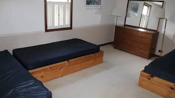 A room with two wooden beds with blue mattresses, a wooden dresser, a floor lamp, and a window with blinds.