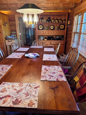 Une salle à manger en bois avec une grande table dressée pour six personnes, entourée de chaises.