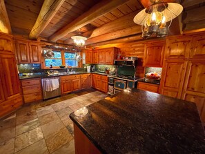 Une cuisine rustique aménagée dans une cabane en bois, avec un grand îlot central, des meubles de rangement en bois et une cuisinière.