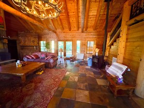 L’intérieur d’une cabane en rondins, avec une cheminée, un canapé en cuir, une table à manger et un escalier.