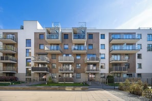 Moderni kerrostalo, jossa on useita parvekkeita, portilla varustettu sisäänkäynti ja päällystetty sisäpiha.