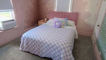 Un dormitorio con una colcha a cuadros, un cabecero rosa y una ventana con persianas.