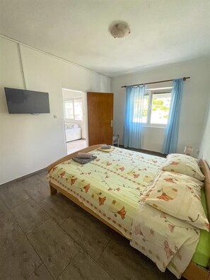 Une chambre à coucher avec un lit, un téléviseur fixé au mur et une fenêtre avec des rideaux.