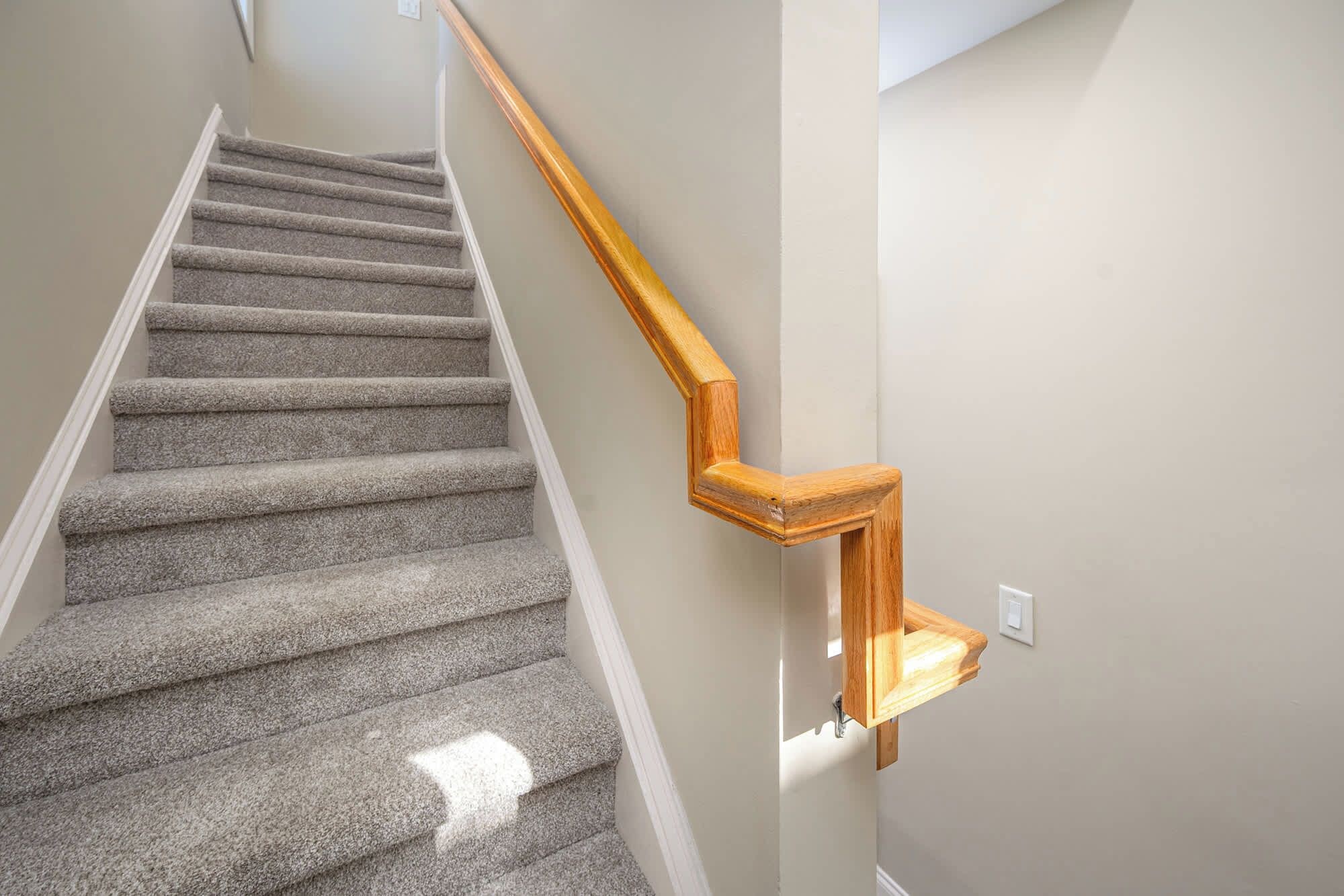 Un escalier recouvert de moquette, avec une main courante en bois.