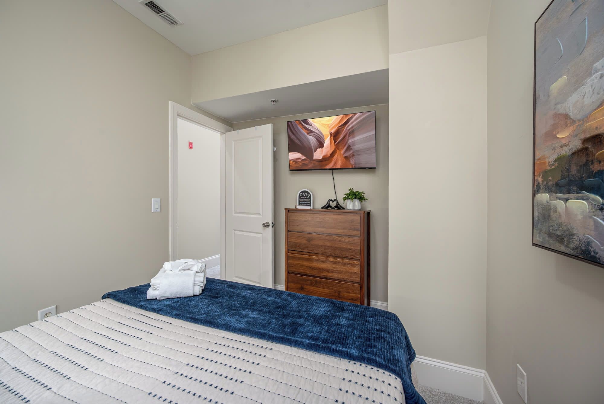 Une chambre à coucher avec un lit, une commode, un tableau et une porte.
