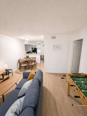 Um apartamento moderno com sala de estar, espaço para refeições, cozinha compacta e mesa de pebolim.