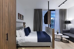 Una habitación de hotel moderna con una cama, un sofá, una mesita y un televisor.