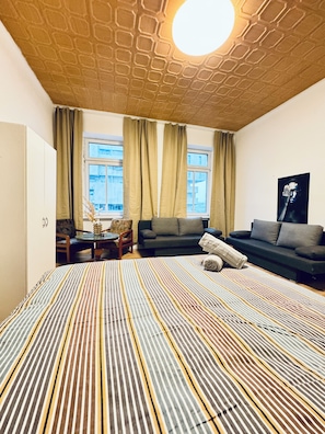 A modern room with a patterned carpet, a sofa, a chair, a small table, and a window with curtains. - The Vienna Quartet Studio for Four (Wien)