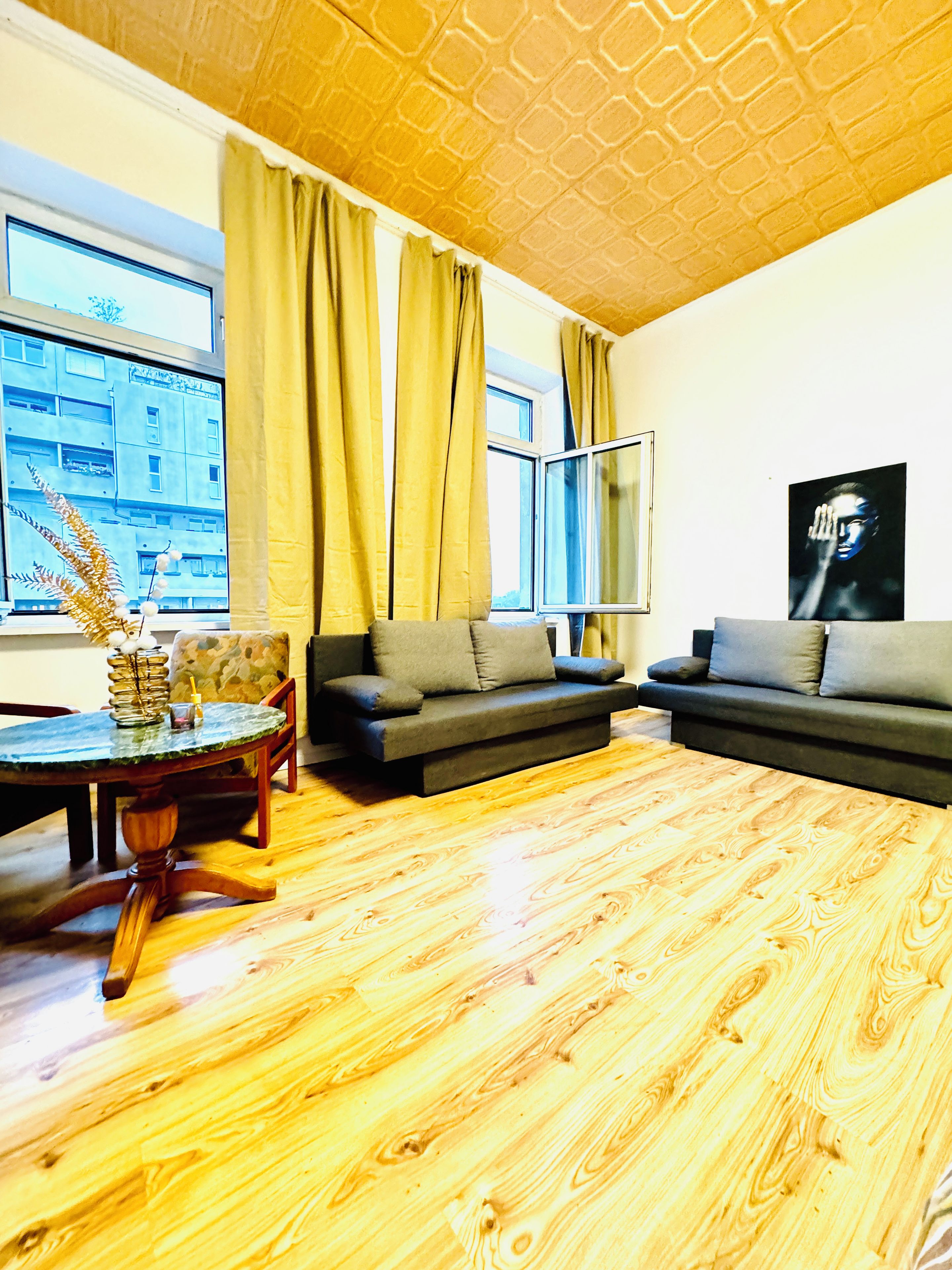 A living room with a wooden floor, two sofas, a round table, and a window with curtains.