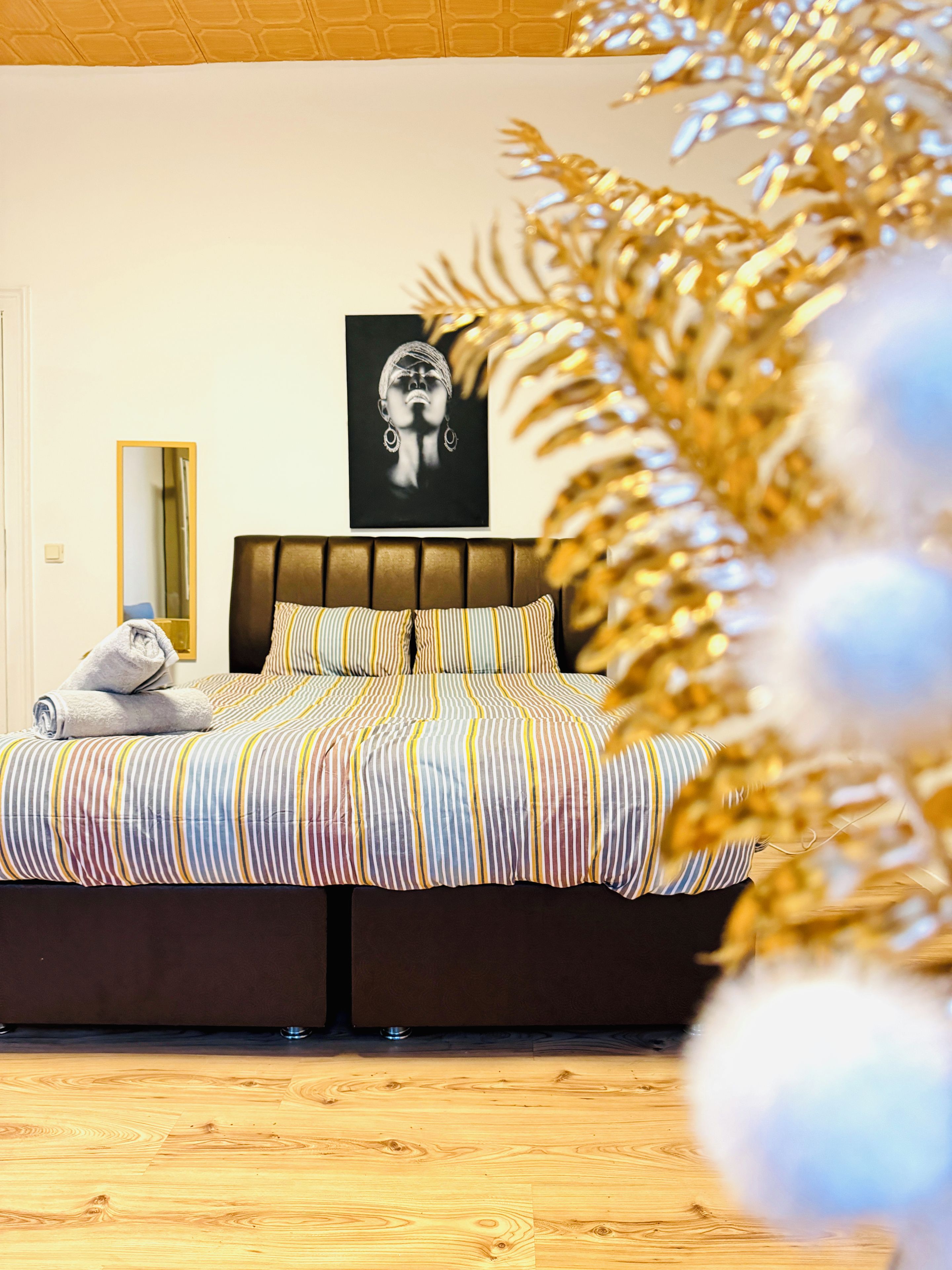 A hotel room with a bed, a framed artwork on the wall, and a wooden floor.