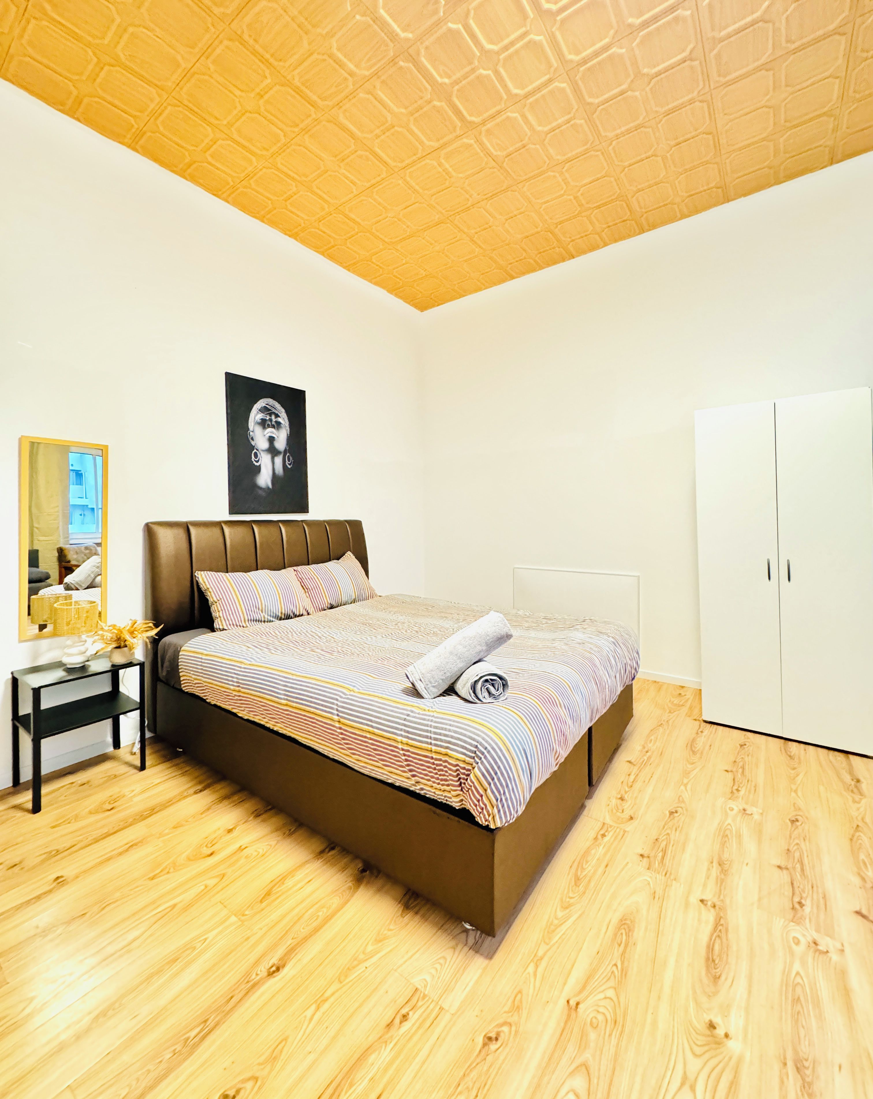 A bedroom with a bed, a wardrobe, a mirror, and a ceiling with a geometric pattern.
