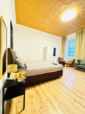 A bedroom with a large bed, a bedside table with a lamp, a chair, and a window with curtains. - The Vienna Quartet Studio for Four (Wien)