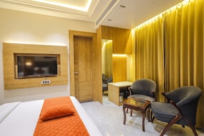 Ein Hotelzimmer mit Bett, Wandfernseher, Schreibtisch mit Stuhl und großem Fenster mit Vorhängen.