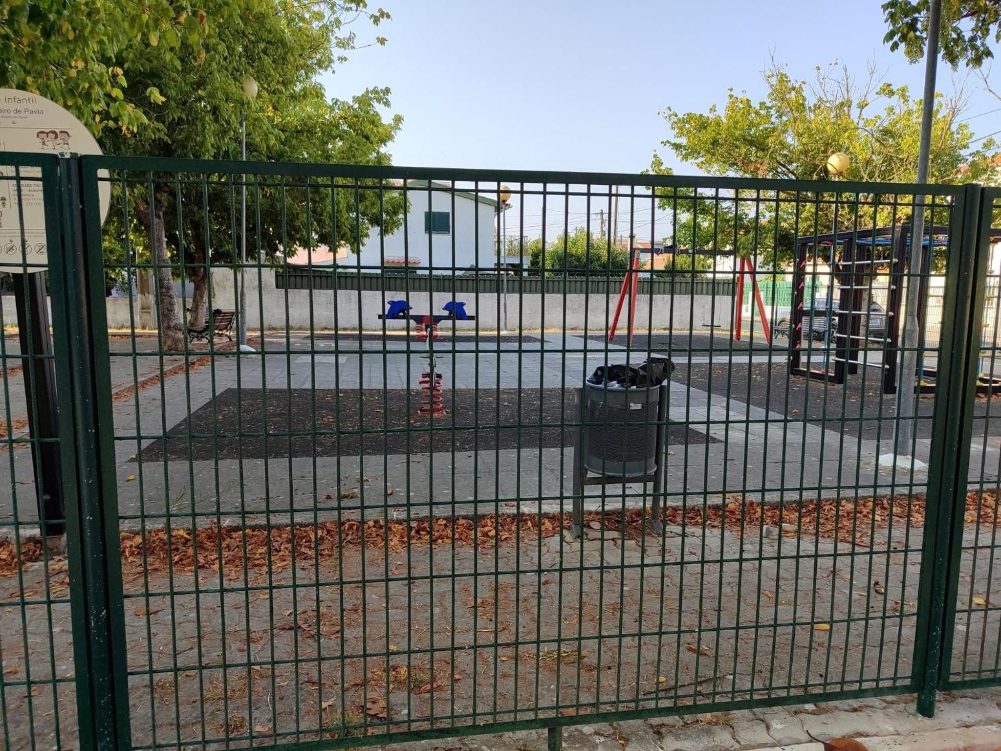 Een omheind speelterrein met een schommel en een klein gebouw op de achtergrond.