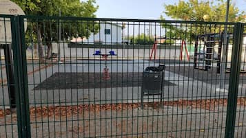 Een omheind speelterrein met een schommel en een klein gebouw op de achtergrond.