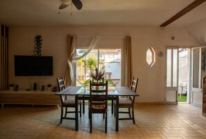 A dining area with a table and chairs, a ceiling fan, a TV mounted on the wall, and a view of the outside. - Aroeira Garden Villa (Aroeira)