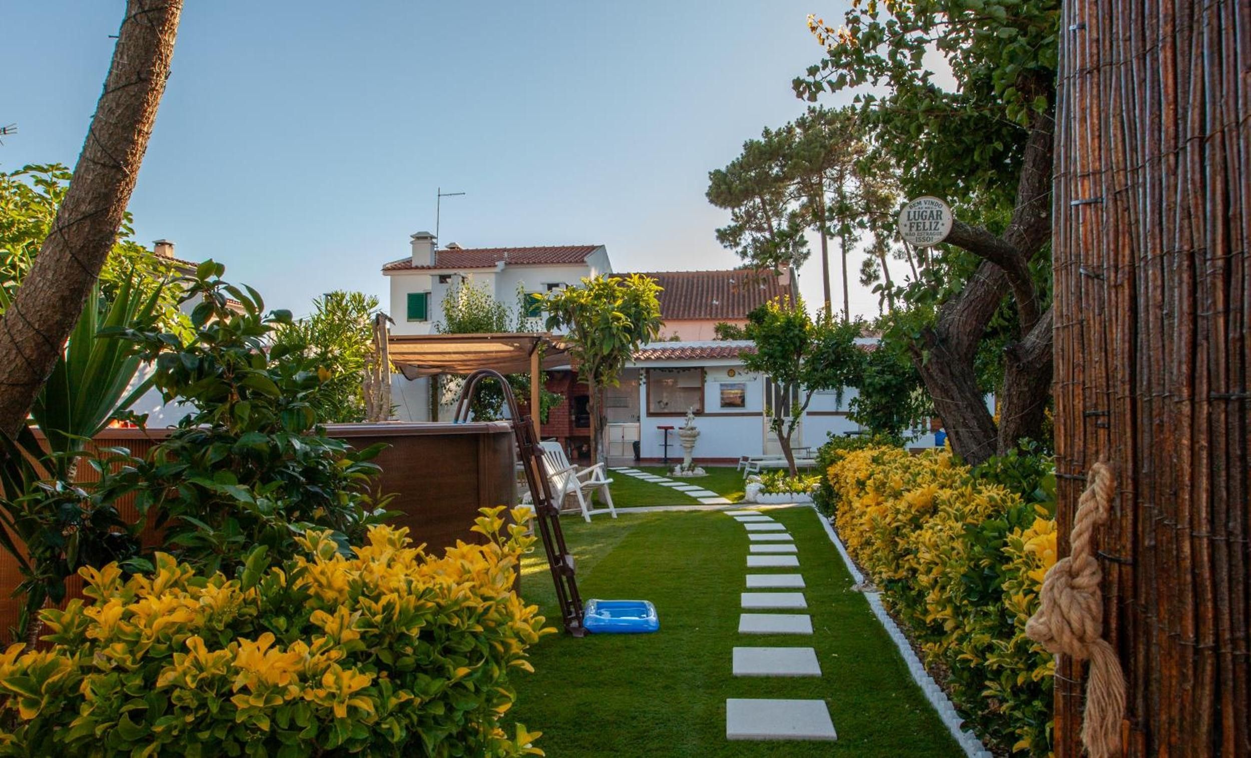 A pathway leading to a building with a tiled roof, surrounded by lush greenery and yellow flowers.