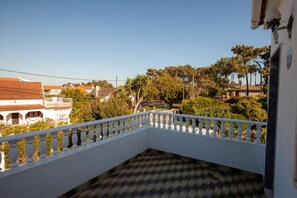 A balcony with a white railing, a tiled floor, and a view of surrounding buildings and trees. - Aroeira Garden Villa (Aroeira)