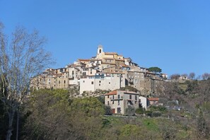 Un pueblo en una colina con una imponente torre de iglesia, edificios escalonados y una mezcla de construcción de piedra y enlucido.