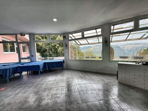 Amplia habitación con grandes ventanales que ofrecen vistas a la montaña, una larga mesa con manteles azules y una encimera de ladrillo.