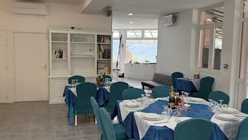 A dining area with tables set for four, teal chairs, and a white cabinet with glassware.