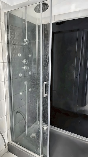 Een douche met glazen wanden, een bedieningspaneel en een donkerdeur.