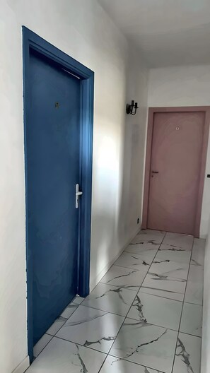 Un pasillo con una puerta azul y una rosa, ambas con manijas. El piso tiene un diseño de mármol.