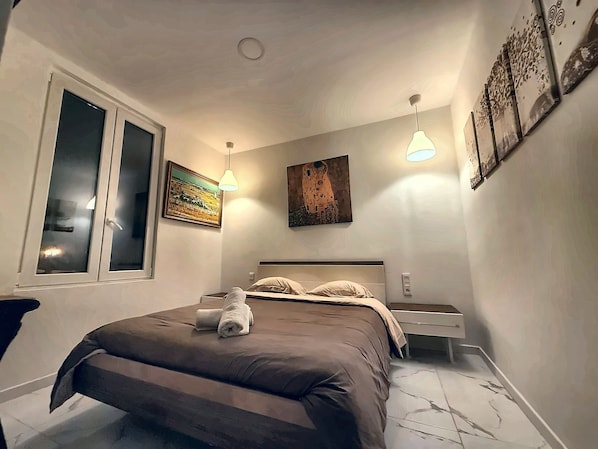 Een slaapkamer met een bed, nachtkastjes, een raam en decoratieve wandkunst.