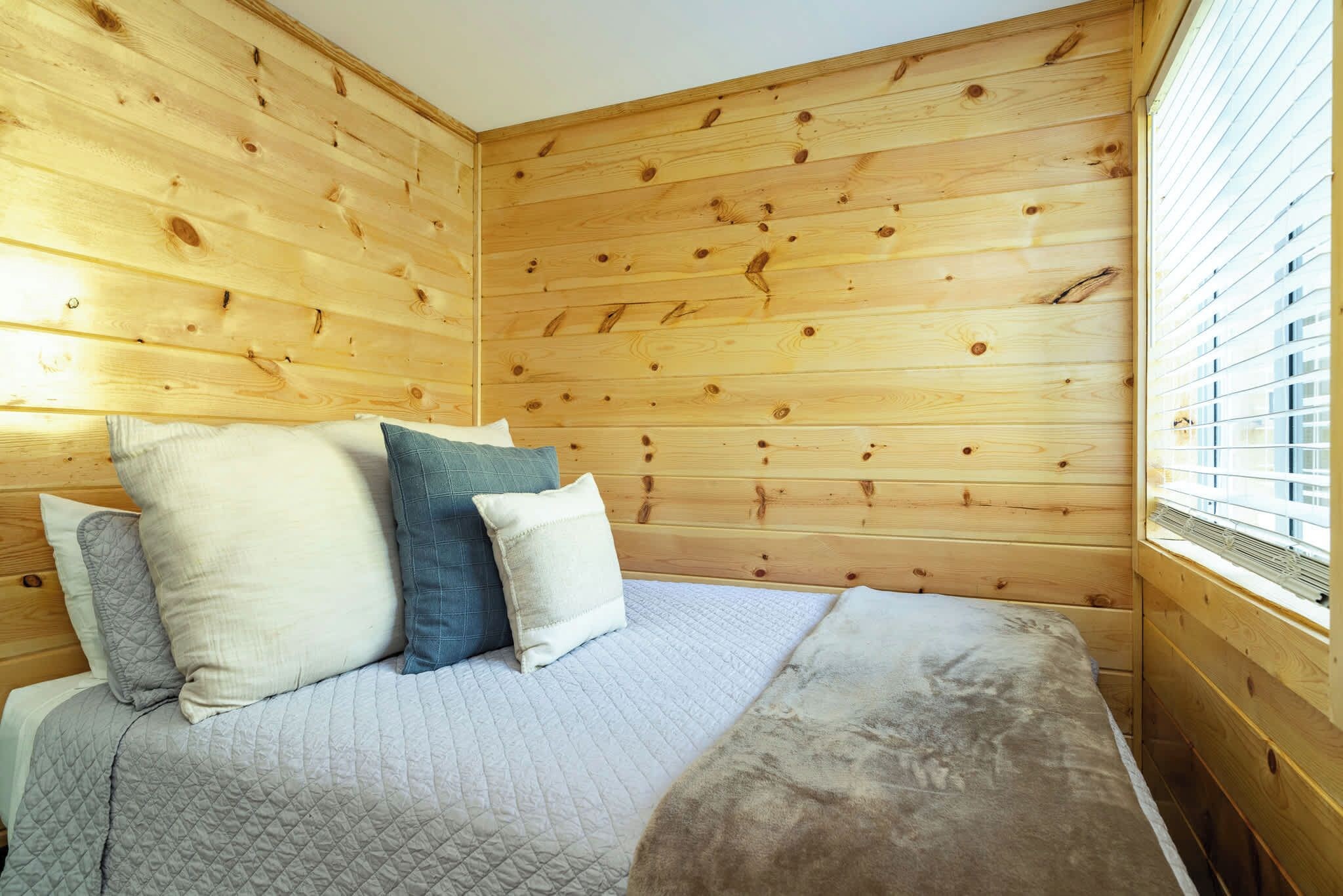 A wooden-paneled room with a bed, pillows, and a window.