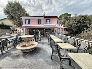 An outdoor seating area with tables and chairs, a fountain, and a building labeled 'HOTEL del ALPI RESTAURANT' in the background. - Bed and Breakfast 'Natura - Chambre 1' with Mountain View, Wi-Fi and Air Conditioning (Berre-les-Alpes)