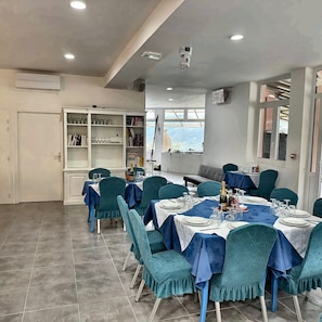 Un área de comedor con mesas dispuestas para una comida, sillas y una estantería al fondo.