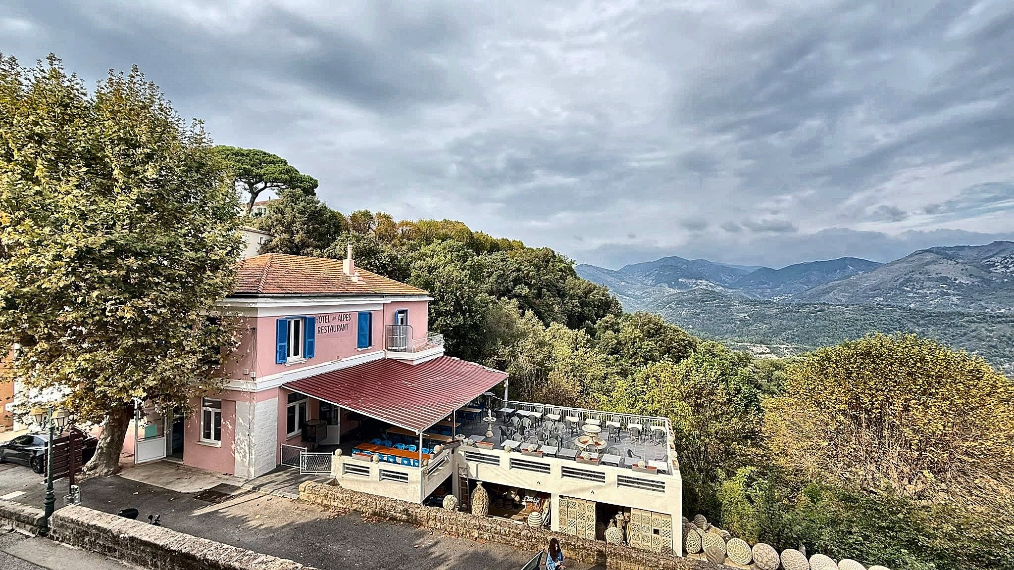 Un edificio rosa con tetto rosso, probabilmente un hotel o un ristorante, con posti a sedere all'aperto e vista sulle montagne.