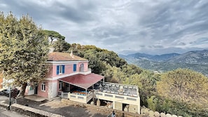Un edificio rosa con techo rojo, posiblemente un hotel o restaurante, con terraza y vistas a las montañas.