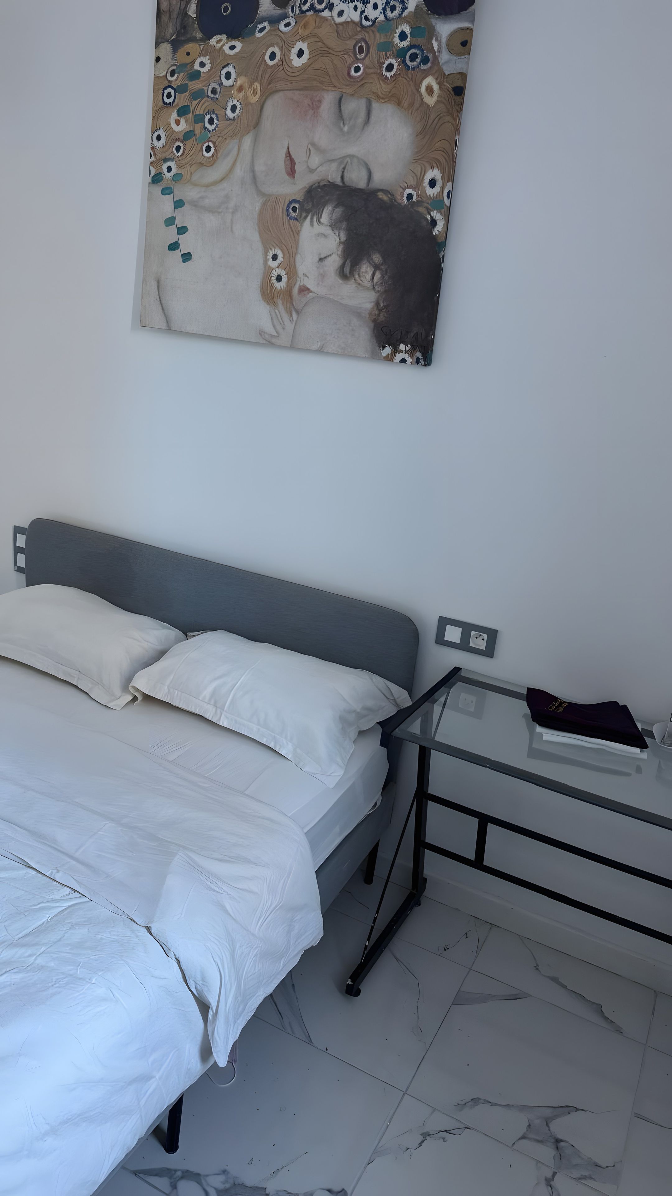 Una camera da letto con un letto, un comodino, un quadro appeso al muro e un pavimento piastrellato.