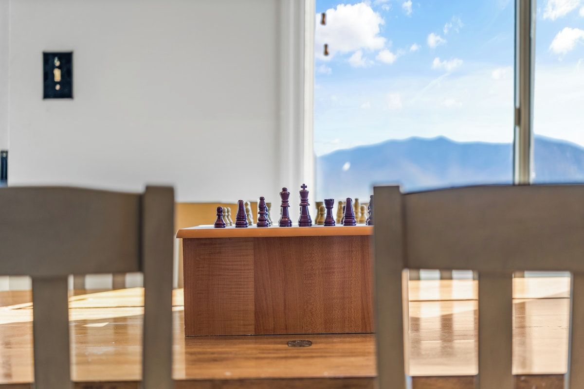 A chessboard on a wooden table with a mountain view through a window.
