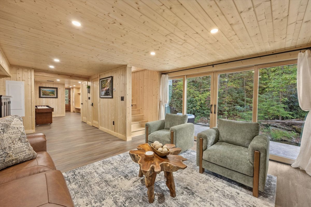 A spacious living area with a wooden ceiling, large windows, and a view of the outdoors.