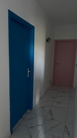 Ein Flur mit einer blauen Tür, einer rosafarbenen Tür und einer Wandleuchte.