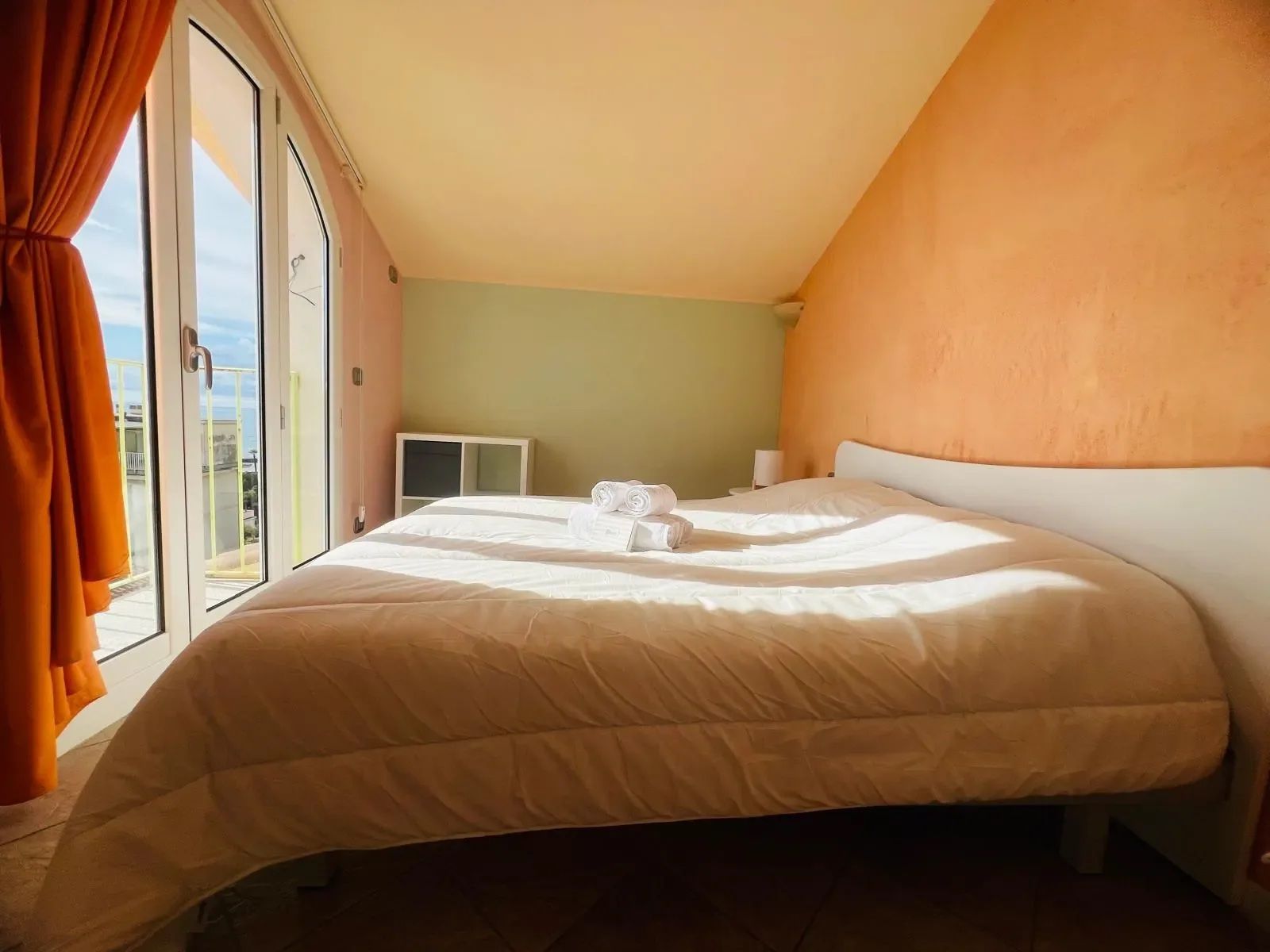 Hotellihuone, jossa on suuri sänky, ikkuna, jossa on verhot, yöpöytä ja näkymä ulos.