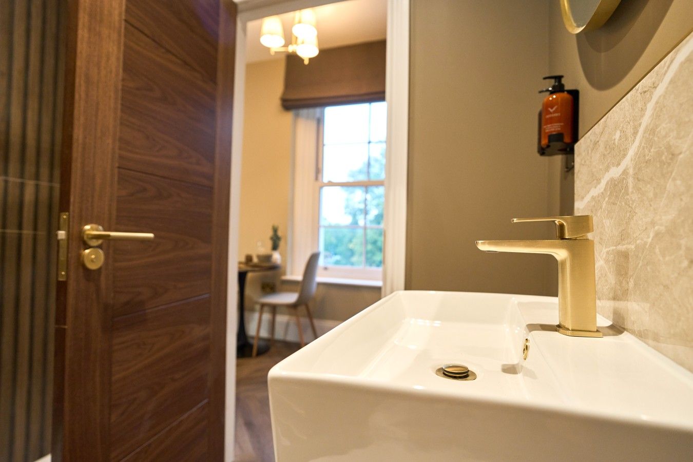 A bathroom with a white sink, gold faucet, and a wooden door.