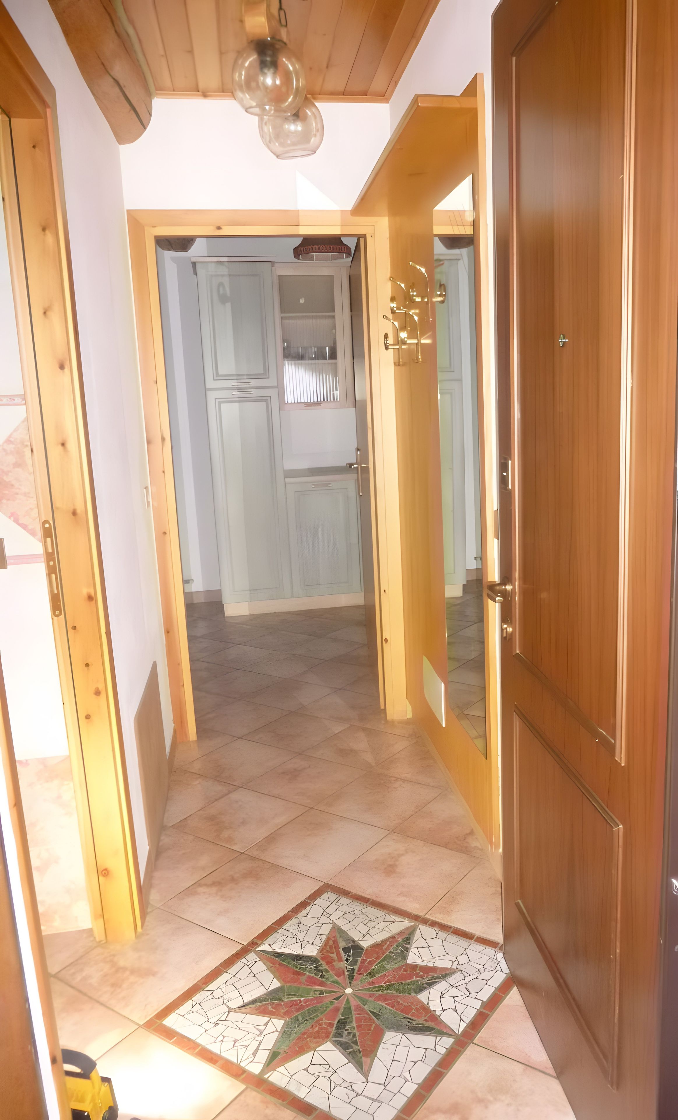 Un couloir avec une porte en bois, un sol carrelé orné d’un motif en étoile et un luminaire au plafond.