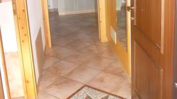Un couloir avec une porte en bois, un sol carrelé orné d’un motif en étoile et un luminaire au plafond.