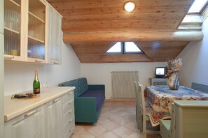 Eine kompakte Küche mit Holzbalkendecke, ein Essbereich mit Tisch und Stühlen, eine Sitzecke und ein Fernseher.