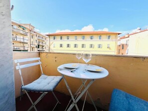 A balcony with a small table and chair, a pair of wine glasses, and a view of buildings in the background. - New Listing (Sanremo)