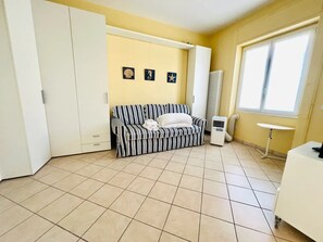 A room with a striped sofa, a small table, a radiator, and a window with curtains. - New Listing (Sanremo)