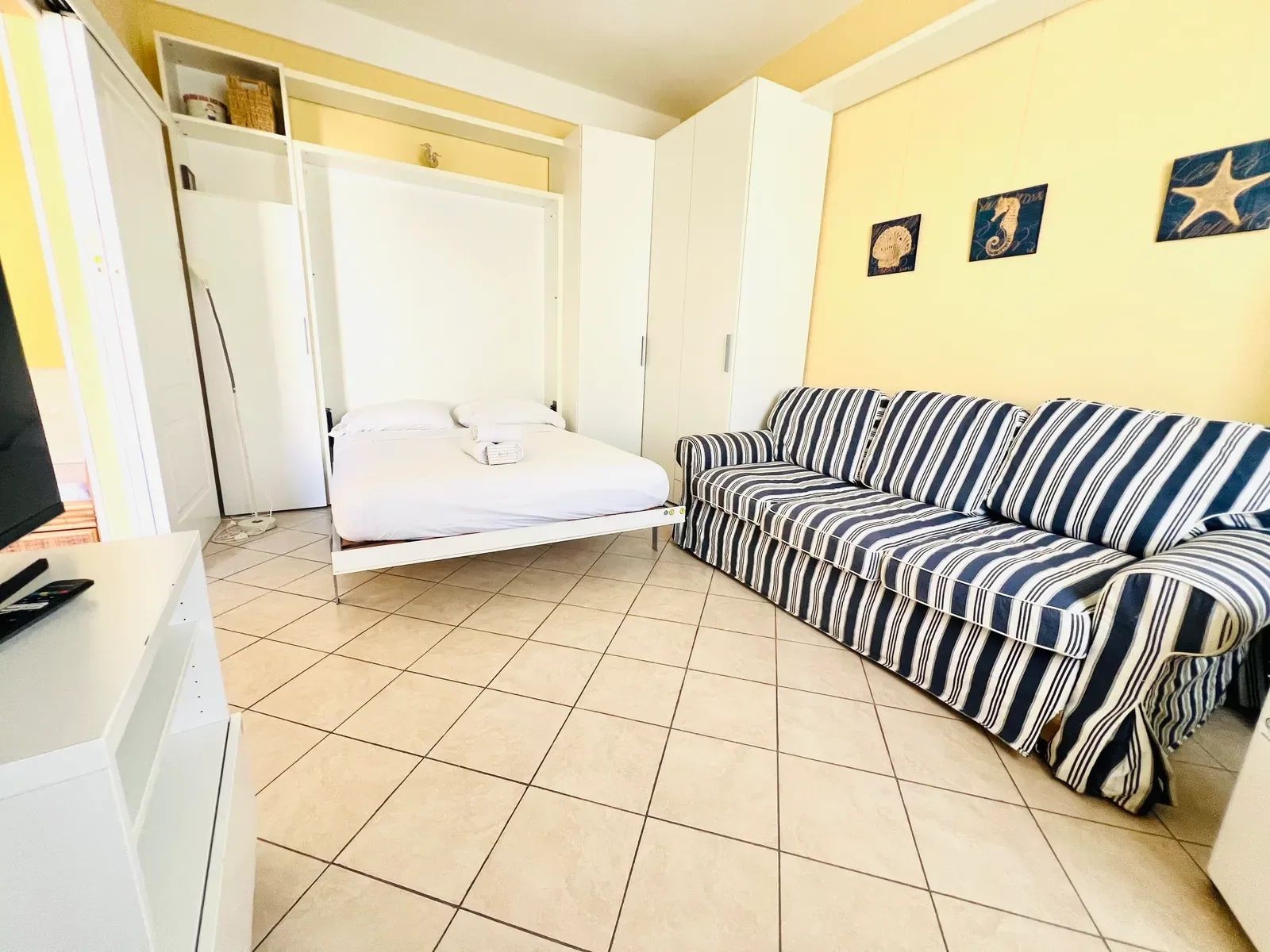 A room with a bed, a striped sofa, a TV, and a wardrobe.