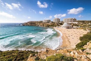 Un hotel a la costa amb diverses edificacions, una platja de sorra i penya-segats rocosos.