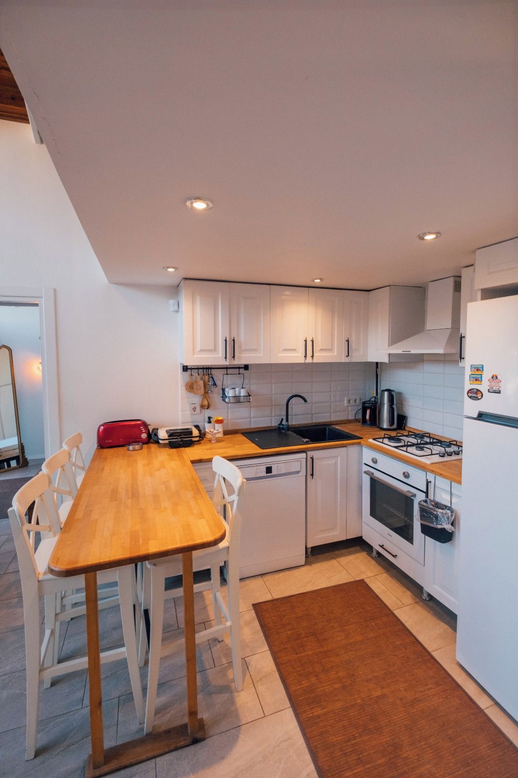 A compact kitchen with white cabinets, a wooden dining table, and a built-in oven.